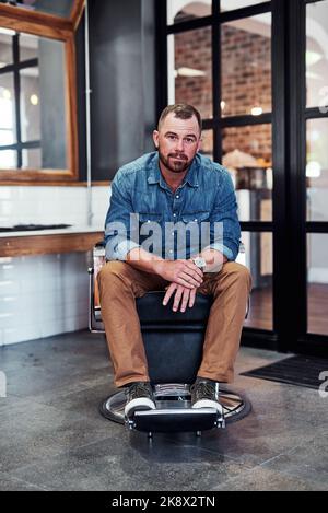 I made it happen, so can you. Full length shot of a handsome mature barber sitting on a chair inside his barbershop. Stock Photo
