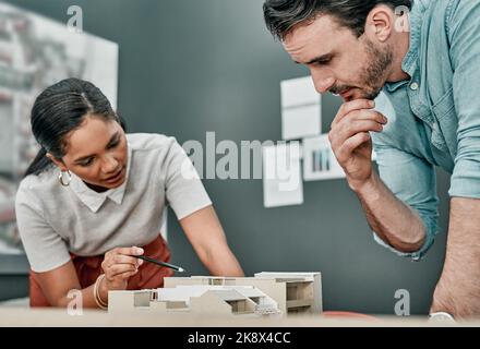 Being a designer means being a problem solver. two architects working together on a scale model of a building in an office. Stock Photo