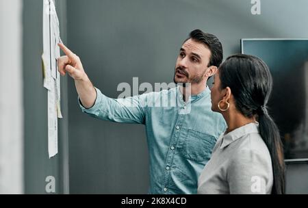 Do we need to make any more changes here. two architects working with blueprints on a wall in an office. Stock Photo