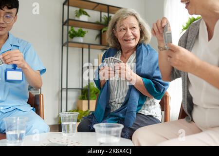 Nursing home patients spending time playing cards with nurse Stock Photo