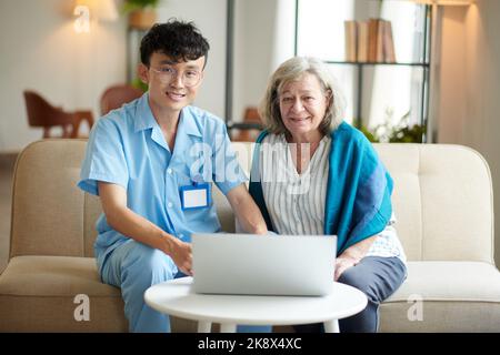 Happy nursing home caregiver teaching senior woman working on laptop and makeing video calls Stock Photo