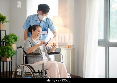 Nursing home worker helping senior patient with application on tablet computer Stock Photo
