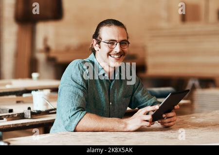 I use social media to market my business. Portrait of a young carpenter using a digital tablet while working inside his workshop. Stock Photo