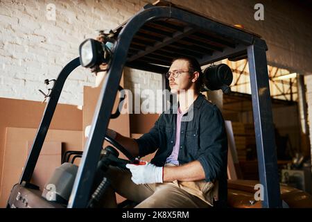 This is how I get around here in the warehouse. a young male warehouse worker driving a forklift. Stock Photo