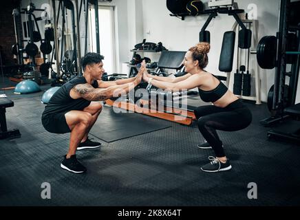 We raise our pain threshold when working out together. two sporty young people working out together at the gym. Stock Photo