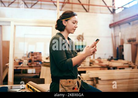 Social media is raving about our unique designs. a female carpenter using her cellphone in her workshop. Stock Photo