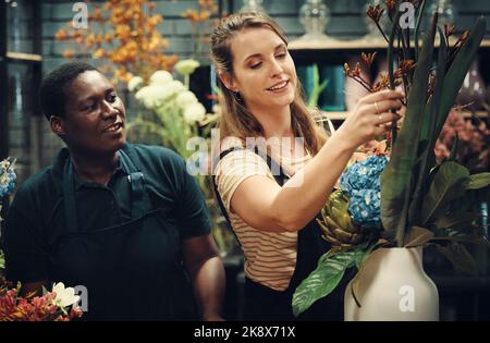 Lets fix this quickly. two attractive young florists standing together and adjusting the flower arrangements in her shop. Stock Photo