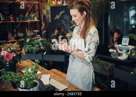 Updating my social media. an attractive young businesswoman standing in her floristry and using her cellphone to photograph her flowers. Stock Photo