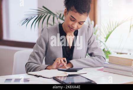 Her finances are looking good. an attractive young businesswoman using a calculator and a notebook while working on her finances in her office. Stock Photo