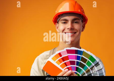 Handsome young worker in uniform holding paint samples palette on yellow background Stock Photo
