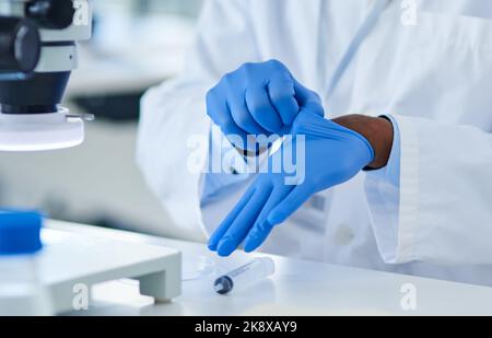 I need to protect my hands for this one. Closeup of an unrecognizable scientist putting protective gloves on while doing experiments inside of a Stock Photo
