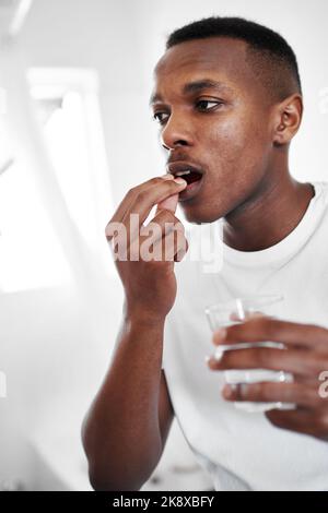 This will give me the boost I need. a young man taking medication at home. Stock Photo