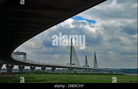 The Mersey Gateway Bridge curves away under fluffy clouds to cross the River Mersey and the Manchester Ship canal between Widnes and Runcorn. Stock Photo