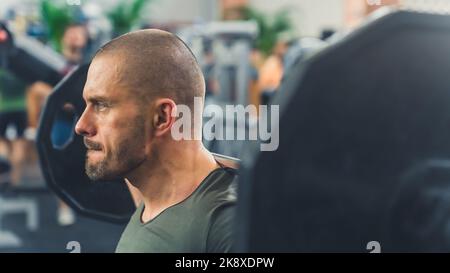 Portrait of focused powerful masculine bald caucasian man with facial hair lifting a barbell and placing it on his neck to do squads. Gym interior: blurred background. High quality photo Stock Photo