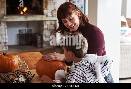 Jack-O-Lantern is the only vegetable he likes. a happy young mother carving out pumpkins and celebrating halloween with her young son at home. Stock Photo