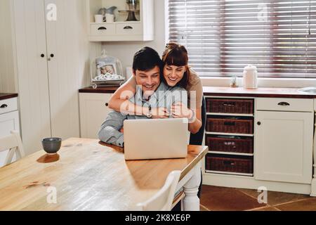What are you looking up. a man using his laptop while being embraced by his wife at home. Stock Photo