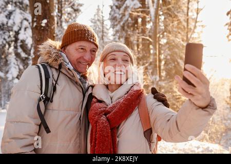 Waist up portrait of happy mature couple taking selfie photo while enjoying hike in winter forest, copy space Stock Photo