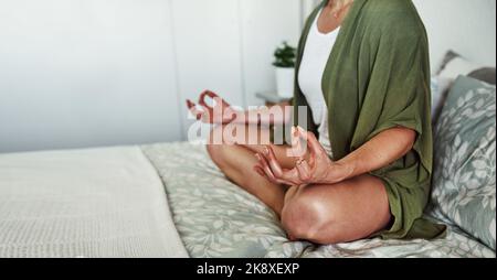 Yoga is good for both your body and mind. an unrecognizable young woman meditating while sitting on her bed at home. Stock Photo