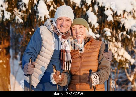 Waist up portrait of happy senior couple looking at camera while hiking in winter forest together Stock Photo