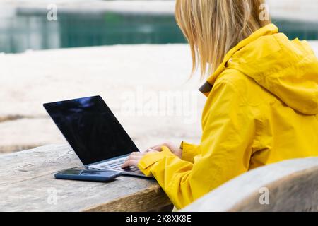 Remote worker relaxing near the lake and using a laptop. Working or studying over a laptop and smartphone. Stock Photo