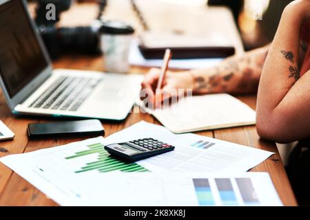 I am always thinking of ways to improve my business. an unrecognizable businesswoman sitting and writing in a notebook after calculating her finances. Stock Photo