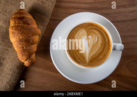 Croissant with in white cappuccino on wooden table Stock Photo