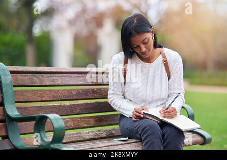 You only pass when you put the work in. a young woman making notes while sitting outdoors. Stock Photo