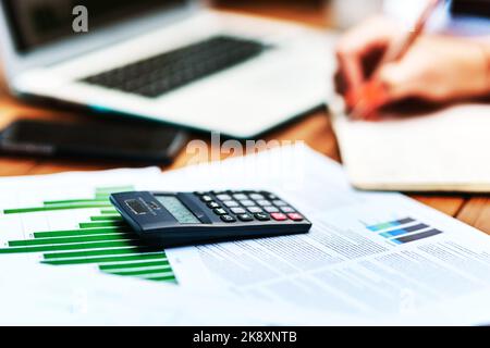 Working out my profits. an unrecognizable businesswoman sitting and writing in a notebook after calculating her finances. Stock Photo