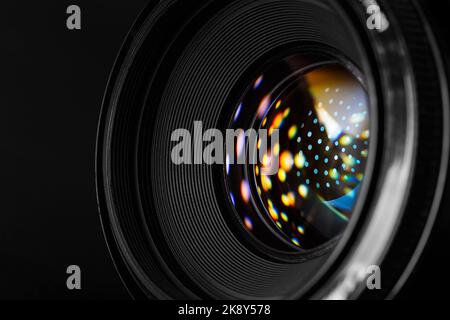 A close-up photographic lens, with multi-colored reflected spots on the surface of the front lens. Macro photography in dark style Stock Photo
