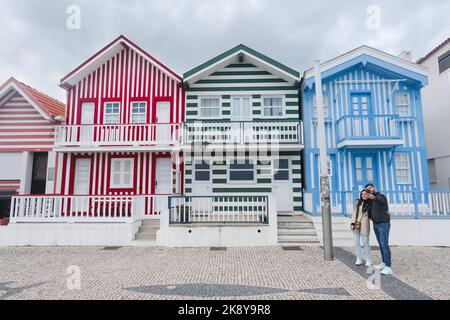 A couple in love taking a selfie on street with typical colorful striped houses called Palheiros. Costa Nova do Prado is a beach village resort on Stock Photo