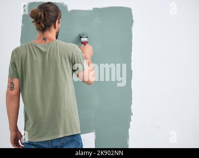Painting, brush and renovation with a man doing interior DIY in a room for improvement and remodel of home. Young man, decoration and work with green Stock Photo