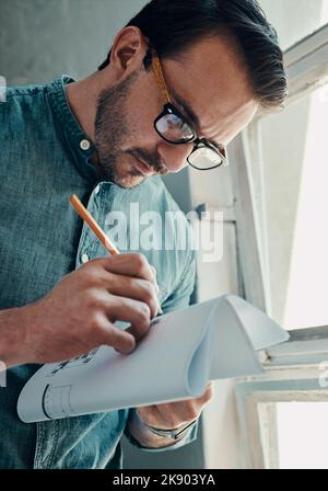 A masterpiece is loading...a handsome young male architect writing on a blueprint while standing in a modern office. Stock Photo