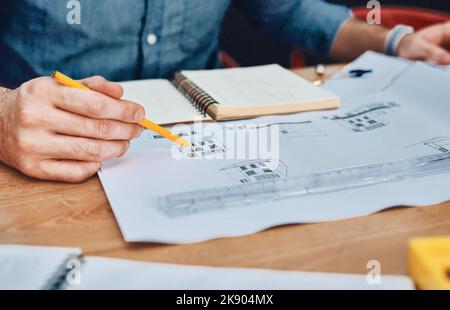 You can count on him for the best designs. an unrecognizable male architect working with blueprints in a modern office. Stock Photo