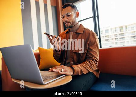Young entrepreneur speaking on the phone and using a laptop in a co-working space. Focused young businessman making plans with his business associates Stock Photo