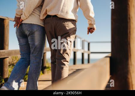 Rearview of a mature couple holding hands while taking a walk along a wooden foot bridge. Romantic elderly couple taking a refreshing beach holiday af Stock Photo
