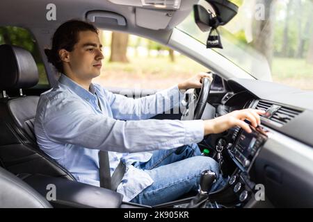 close up of young man in suit driving car and switching some button on panel of car Stock Photo