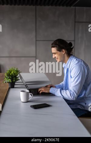 Smiling young man working on laptop in modern kitchen, checking email in morning, writing message in social network, happy young male using internet b Stock Photo