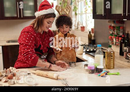 We both have messy hands. a cheerful young woman and her son baking cookies together in the kitchen during christmas time at home. Stock Photo