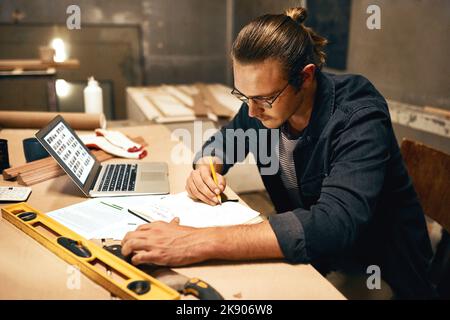I have to think carefully about this. a focused young male carpenter working on a project inside of a workshop at night. Stock Photo