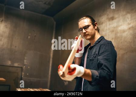 It seems to be the right length. a focused young male carpenter holding and examining a piece of wood while working inside of a workshop at night. Stock Photo