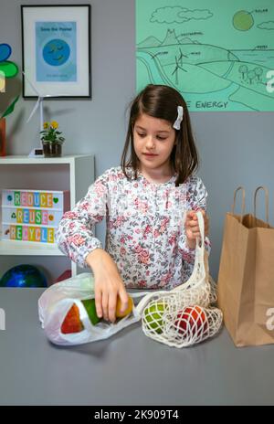 Student taking fruits from disposable plastic bag to reusable mesh bag in ecology classroom Stock Photo