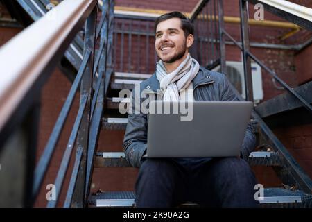 stylish business man with a laptop on his knees sitting on the stairs in the office, Entrepreneurship development and business planning concept Stock Photo