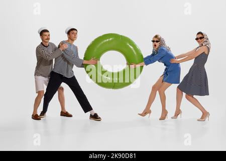 Portrait of two stylish young women pulling big swimming circle with seamen over white background. Stock Photo