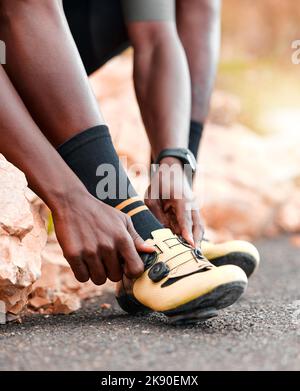 Black man, cycling shoes and fitness in sports motivation for cardio exercise, training or workout in the outdoors. African American male tying shoe Stock Photo