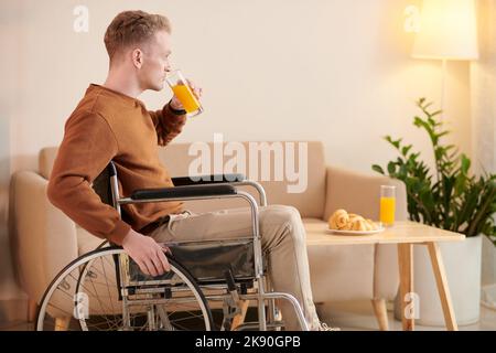 Young man sitting in wheelchair drinking glass of orange juice Stock Photo