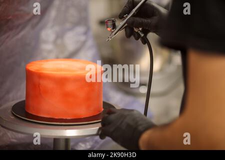 cook preparing a red frosted cake using air bush Stock Photo