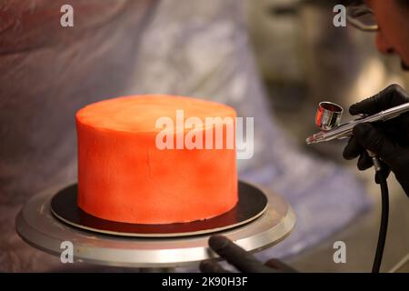 cook preparing a red frosted cake using air bush Stock Photo