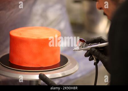 cook preparing a red frosted cake using air bush Stock Photo