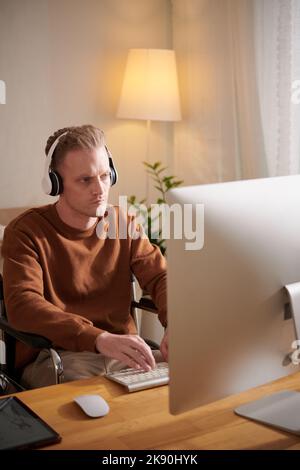 Serious young man wearing headphones when working on computer at desk Stock Photo