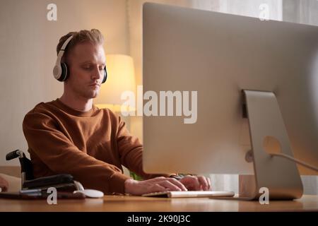 Young man in wheelchair working on computer or playing videogame at home Stock Photo